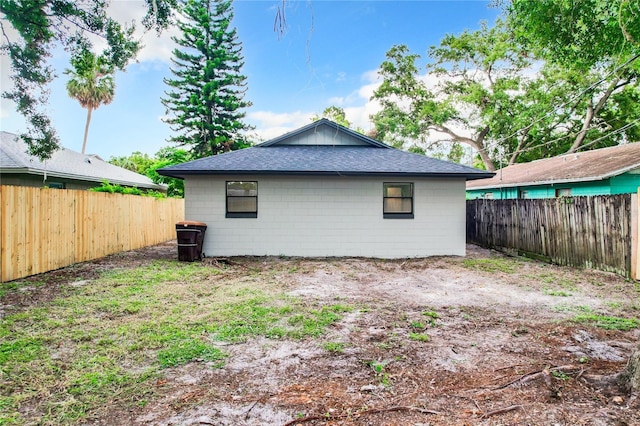 view of home's exterior with concrete block siding, a fenced backyard, and roof with shingles