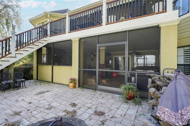 rear view of property with a patio, stairway, a sunroom, and stucco siding