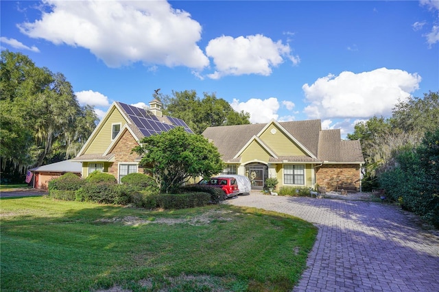 view of front facade featuring solar panels, decorative driveway, and a front yard