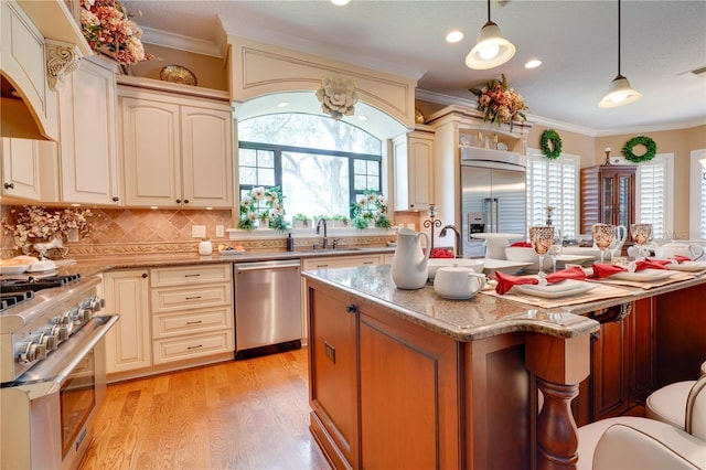 kitchen featuring light wood finished floors, high quality appliances, crown molding, cream cabinetry, and a sink