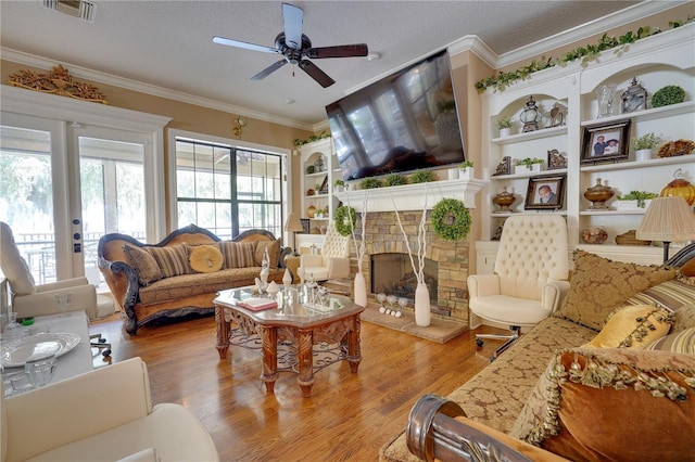 living area featuring visible vents, ornamental molding, wood finished floors, a textured ceiling, and a fireplace