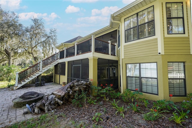 rear view of house featuring an outdoor fire pit, a patio, a sunroom, stairs, and stucco siding