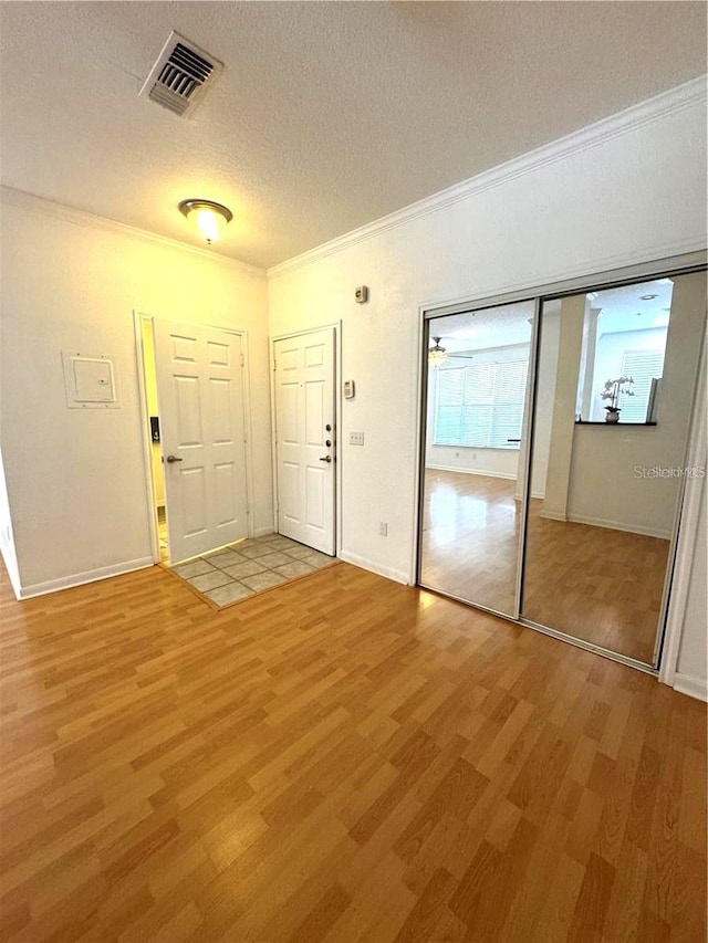 foyer with ornamental molding, a textured ceiling, and light hardwood / wood-style flooring