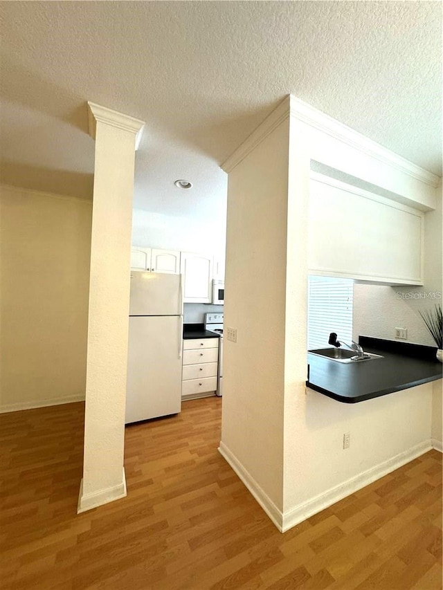 hallway featuring a textured ceiling, sink, decorative columns, and light hardwood / wood-style floors