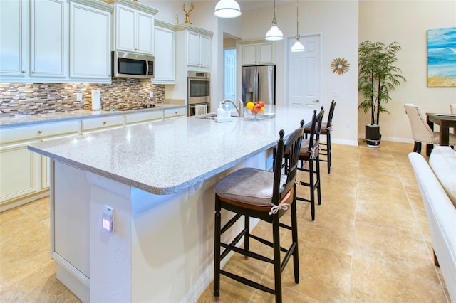 kitchen with stainless steel appliances, sink, an island with sink, pendant lighting, and tasteful backsplash