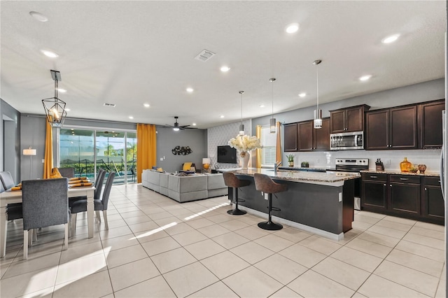 kitchen featuring light stone countertops, pendant lighting, appliances with stainless steel finishes, a kitchen island with sink, and ceiling fan