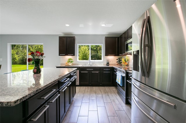 kitchen featuring stainless steel appliances, a center island, light wood-type flooring, and light stone countertops