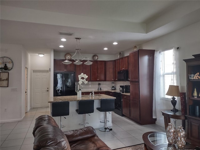 kitchen featuring backsplash, light tile patterned floors, black appliances, an island with sink, and a kitchen bar