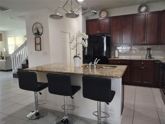 kitchen with light tile patterned floors, black fridge with ice dispenser, sink, an island with sink, and tasteful backsplash