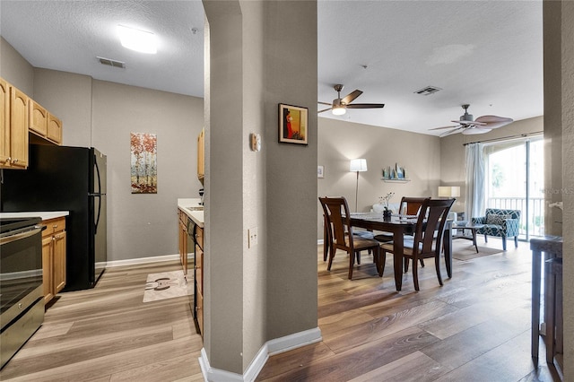 kitchen featuring light wood-type flooring, a textured ceiling, stainless steel range, ceiling fan, and light brown cabinets