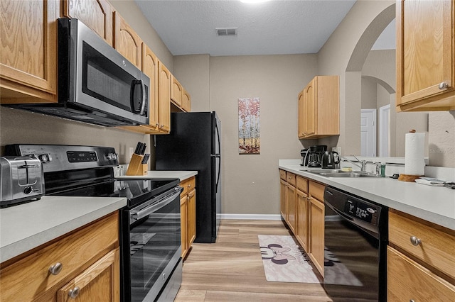 kitchen featuring a textured ceiling, black appliances, sink, and light hardwood / wood-style floors