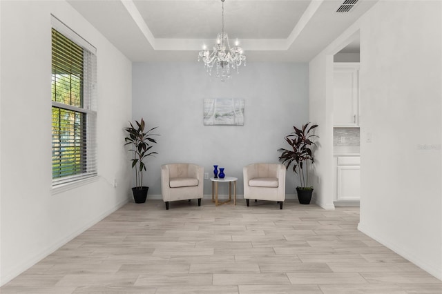 unfurnished room featuring a tray ceiling, light hardwood / wood-style floors, and a notable chandelier