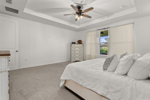 bedroom with light carpet, a tray ceiling, and ceiling fan