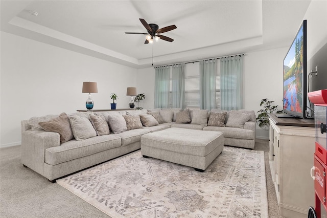 living room with a raised ceiling, ceiling fan, and light colored carpet