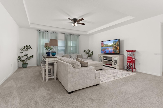 living room with a raised ceiling, light carpet, and ceiling fan