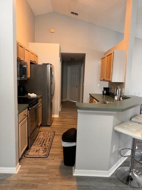 kitchen featuring kitchen peninsula, black electric range, hardwood / wood-style flooring, a breakfast bar area, and vaulted ceiling