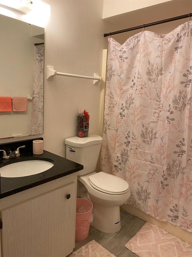 bathroom with hardwood / wood-style flooring, toilet, walk in shower, and vanity