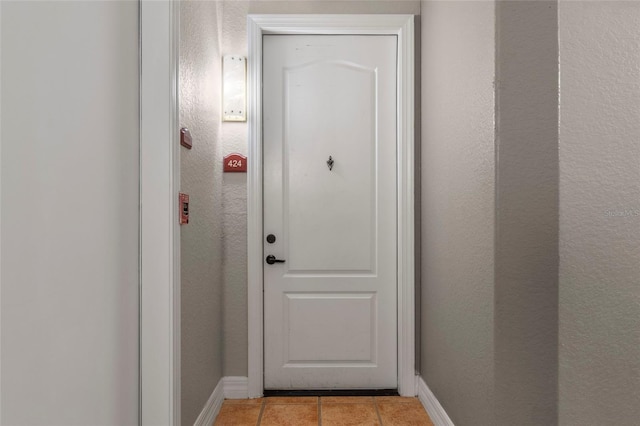 entryway featuring light tile patterned floors, a textured wall, and baseboards