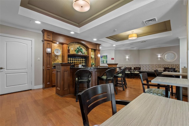 bar with visible vents, backsplash, light wood-type flooring, and a tray ceiling