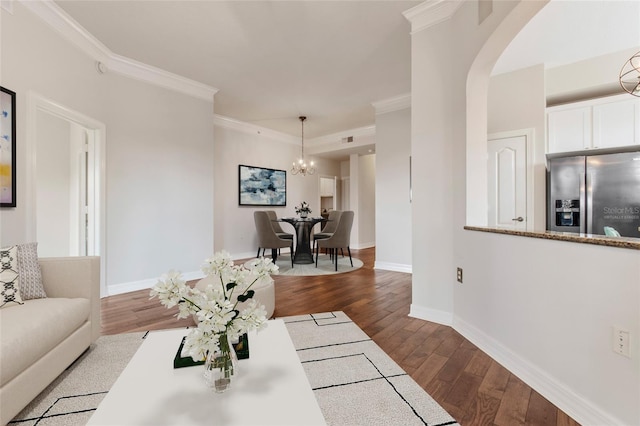 living area featuring ornamental molding, dark wood finished floors, arched walkways, baseboards, and a chandelier