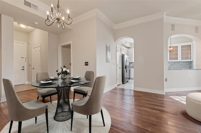 dining space with light wood finished floors, visible vents, baseboards, an inviting chandelier, and arched walkways