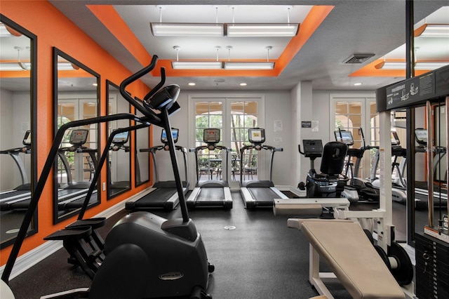 gym with a raised ceiling, french doors, and visible vents