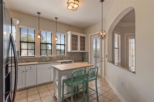 kitchen with a sink, decorative backsplash, glass insert cabinets, stainless steel refrigerator with ice dispenser, and wood counters