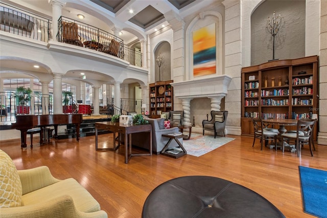 living room with beam ceiling, coffered ceiling, wood finished floors, a high ceiling, and ornate columns