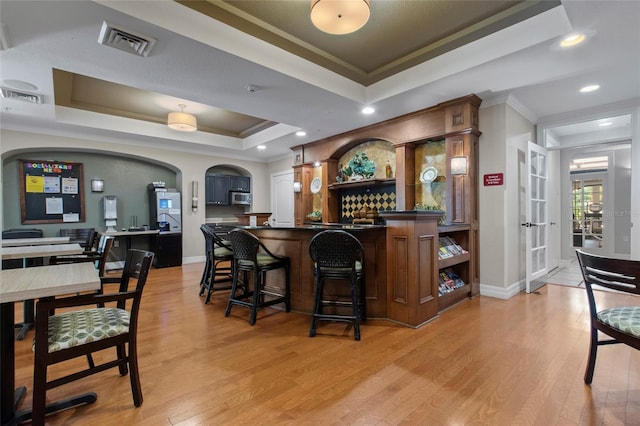 bar with a tray ceiling, light wood-style floors, visible vents, and stainless steel microwave