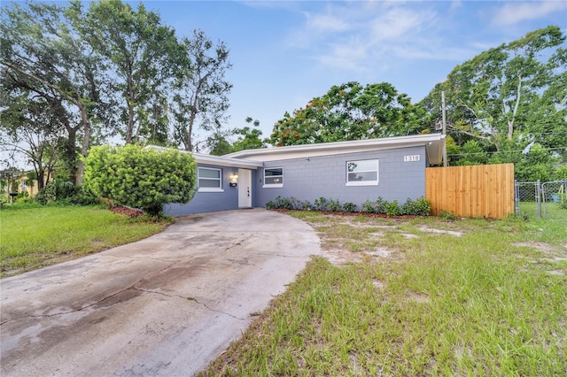 view of front facade featuring driveway, a front lawn, concrete block siding, and fence