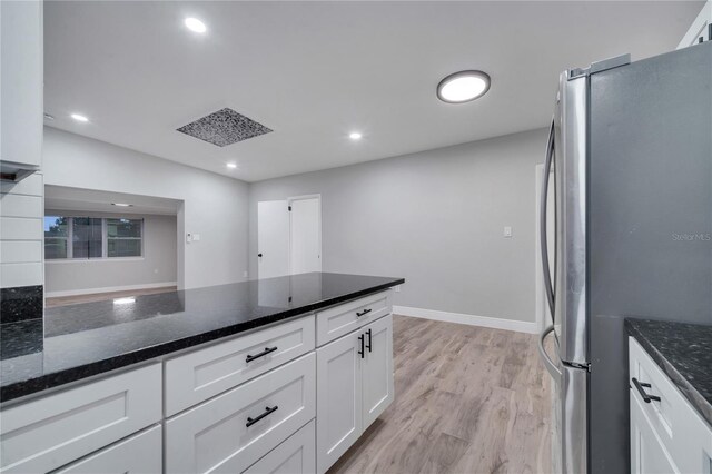 kitchen with light wood-type flooring, stainless steel fridge, white cabinetry, and dark stone counters