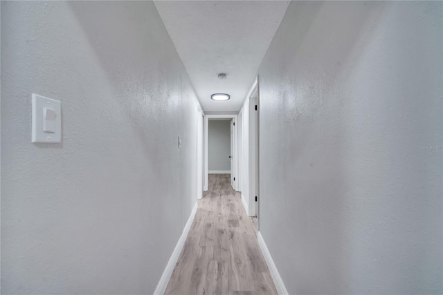 hallway with a textured wall, light wood finished floors, and baseboards