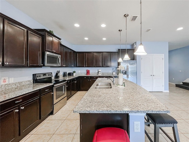 kitchen featuring a kitchen breakfast bar, hanging light fixtures, stainless steel appliances, and a center island with sink