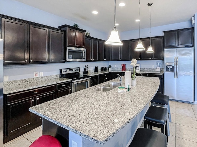 kitchen with sink, a kitchen bar, hanging light fixtures, stainless steel appliances, and a center island with sink