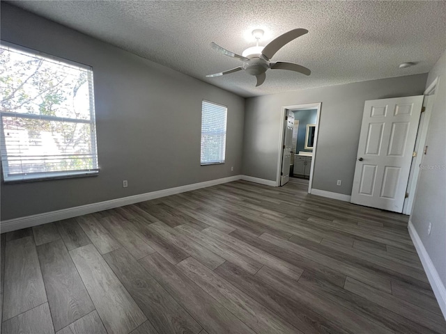 unfurnished bedroom featuring a textured ceiling, ensuite bath, dark wood finished floors, and baseboards