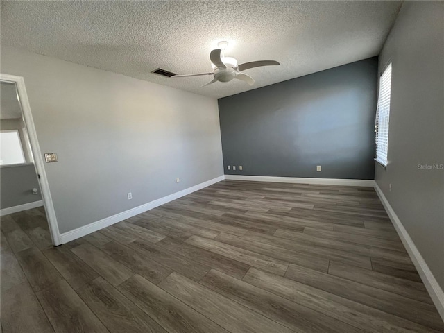 spare room featuring a textured ceiling, dark wood-style flooring, visible vents, a ceiling fan, and baseboards