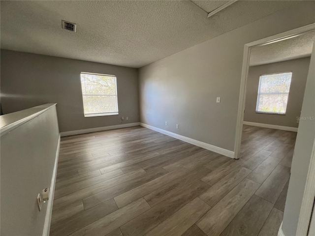 empty room with baseboards, a textured ceiling, visible vents, and wood finished floors