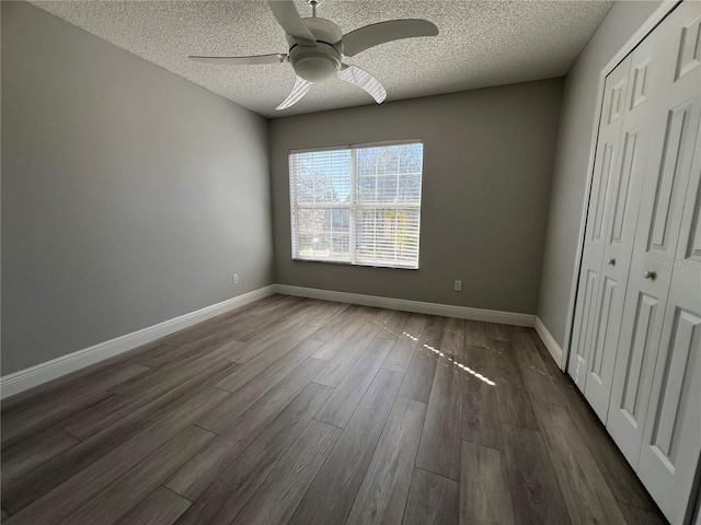 unfurnished bedroom featuring dark wood-style floors, a closet, a textured ceiling, and baseboards