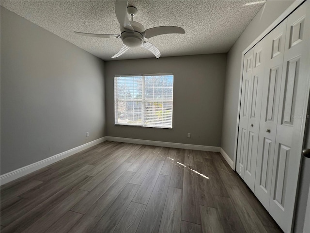 unfurnished bedroom with dark wood-style floors, a closet, a textured ceiling, and baseboards