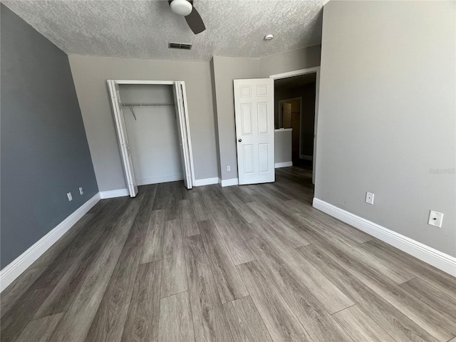 unfurnished bedroom featuring a textured ceiling, a closet, baseboards, and wood finished floors