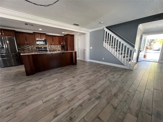 kitchen with crown molding, visible vents, stainless steel microwave, open floor plan, and refrigerator with ice dispenser