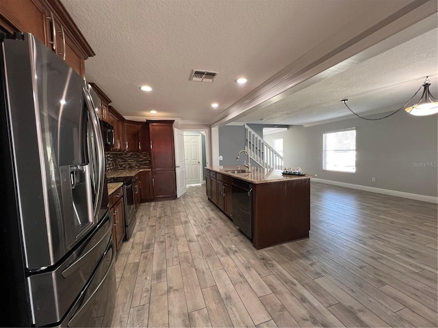 kitchen featuring light wood finished floors, stainless steel appliances, visible vents, decorative backsplash, and a sink