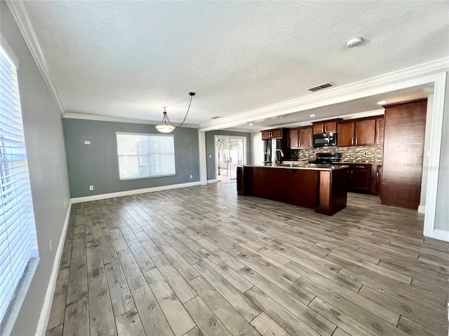 kitchen with light wood-style flooring, visible vents, open floor plan, decorative backsplash, and stainless steel microwave