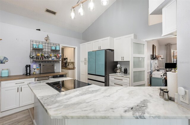 kitchen featuring light hardwood / wood-style flooring, light stone countertops, white cabinetry, stainless steel refrigerator, and high vaulted ceiling