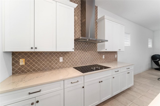 kitchen featuring black electric stovetop, white cabinetry, tasteful backsplash, light stone counters, and wall chimney exhaust hood