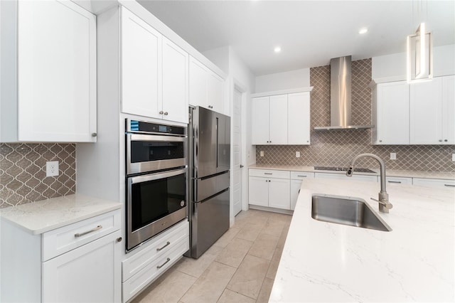 kitchen featuring wall chimney exhaust hood, appliances with stainless steel finishes, tasteful backsplash, hanging light fixtures, and sink