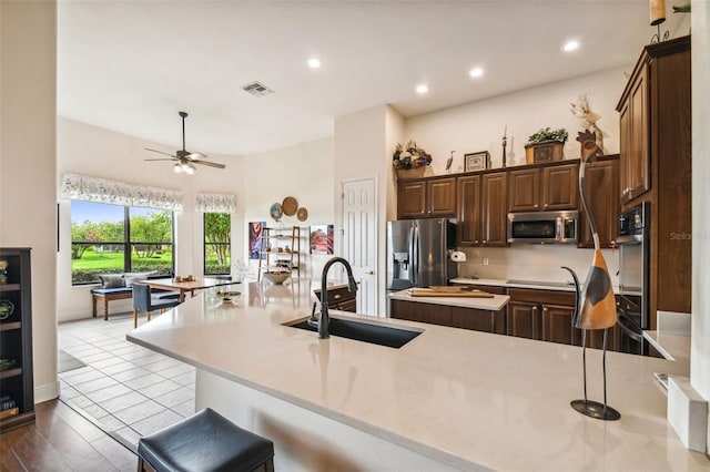 kitchen with light wood-type flooring, dark brown cabinets, stainless steel appliances, sink, and ceiling fan