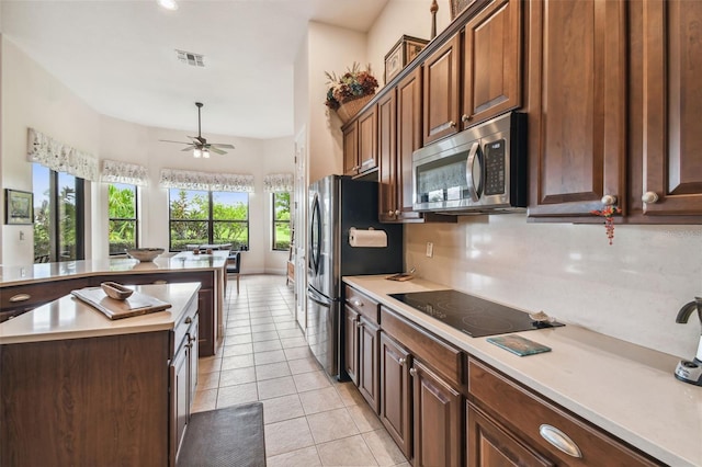 kitchen with appliances with stainless steel finishes, a kitchen island, light tile patterned floors, and ceiling fan