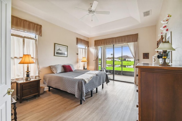 bedroom featuring a tray ceiling, access to outside, ceiling fan, and light hardwood / wood-style floors