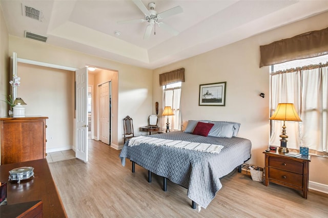 bedroom featuring a raised ceiling, a closet, ceiling fan, and light hardwood / wood-style floors